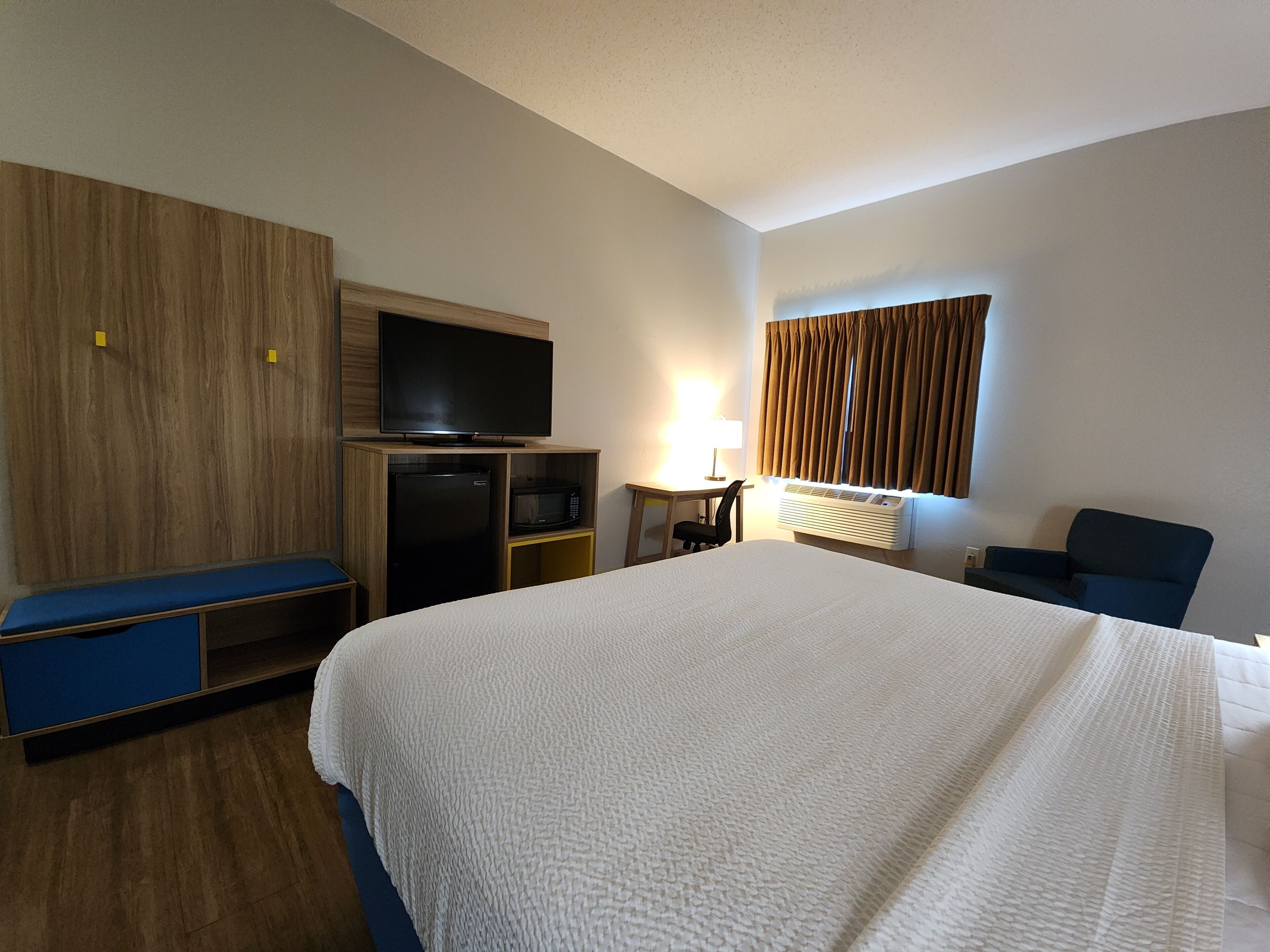 Habitación de hotel con una cama grande, un televisor de pantalla plana, un escritorio con silla, un microondas y un calentador.