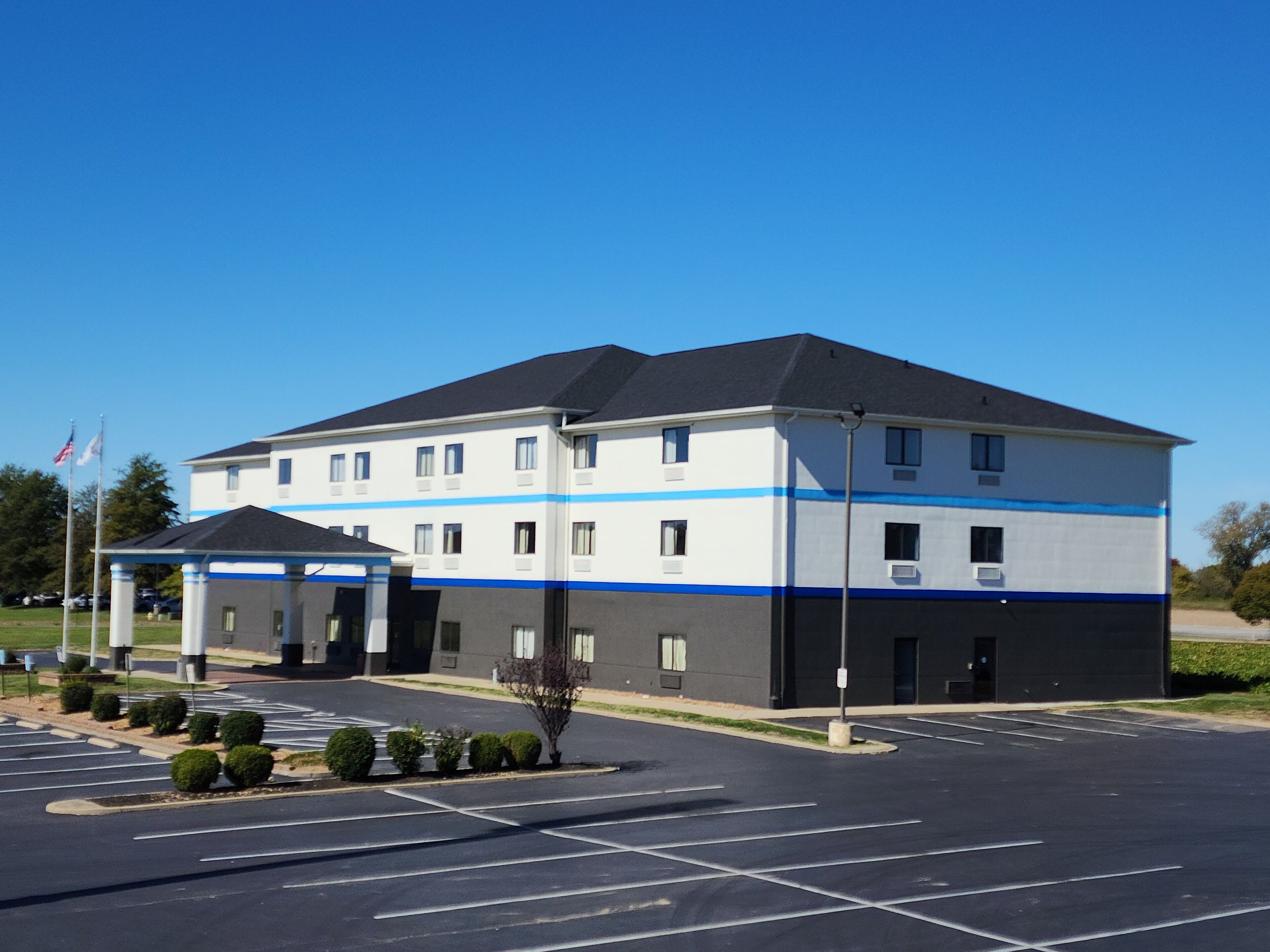 A multi-story hotel with a blue and white facade, a covered entrance, and a parking lot.