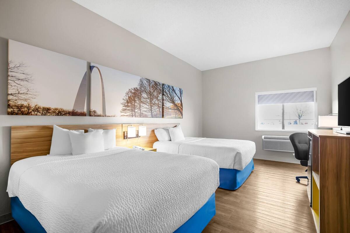 A hotel room with two beds, a desk, a chair, and a large window.