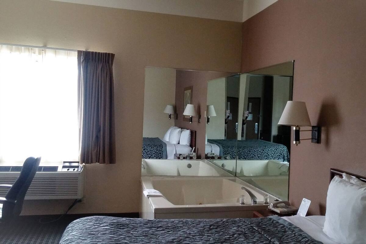 A hotel room with a bed, a desk, a chair, a bathroom with a mirror, and a window with curtains.