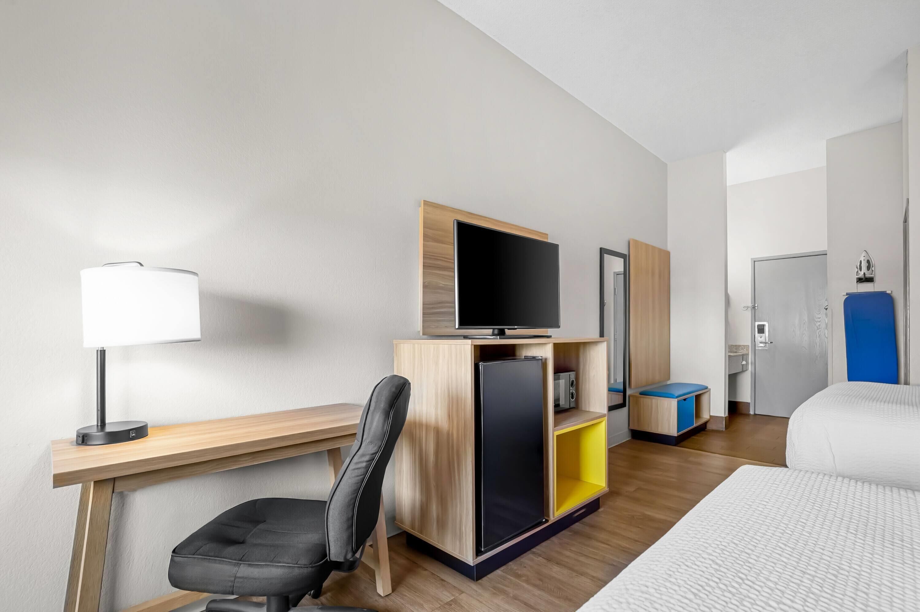 Habitación de hotel con escritorio, silla, televisor, armario y cama.