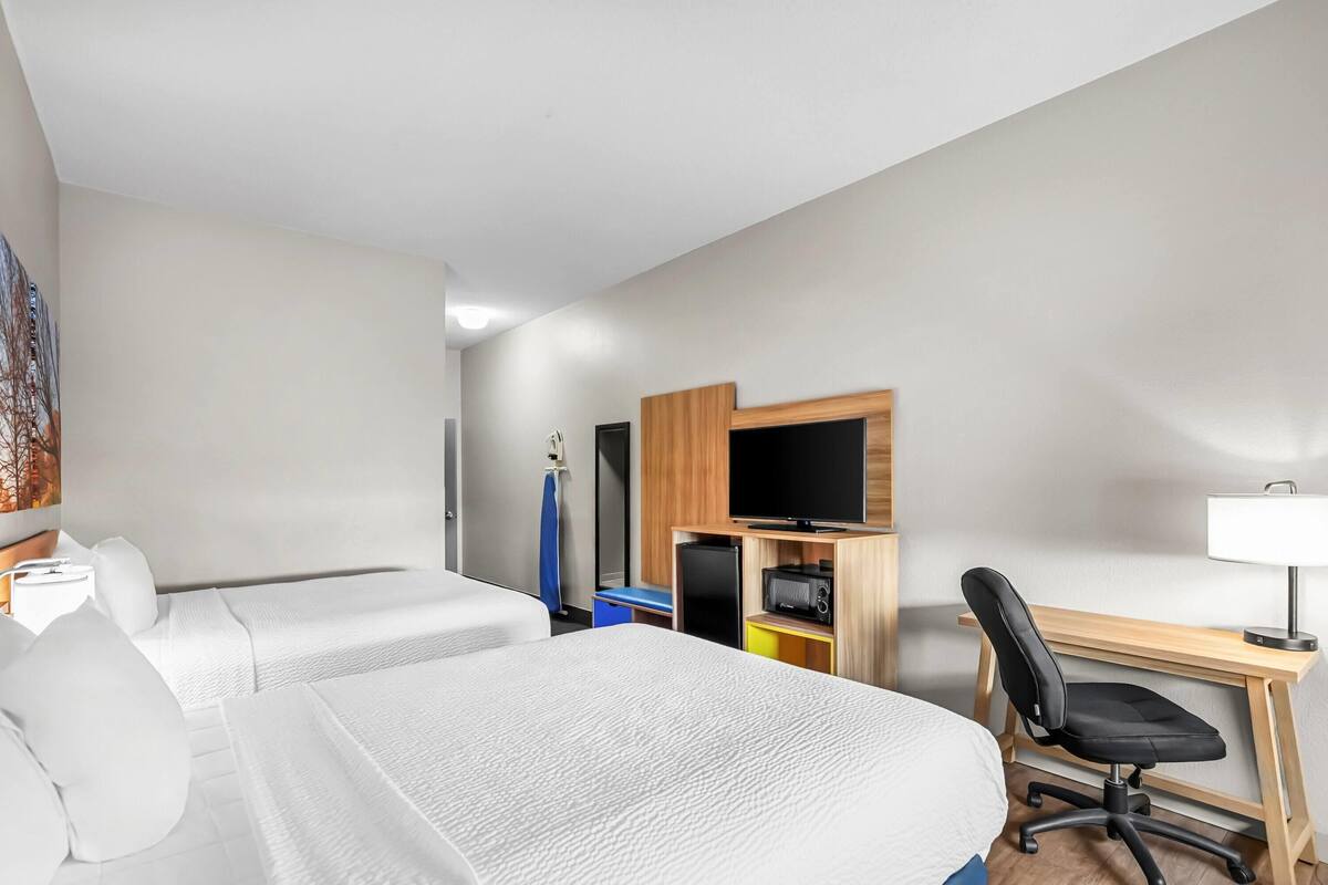 A hotel room with two beds, a desk with a computer, a TV, and a chair.