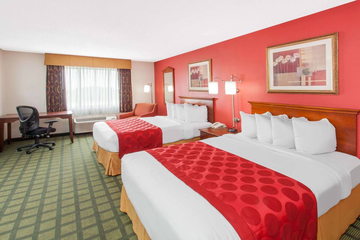 A hotel room with two beds, a desk, a chair, and a window with curtains.