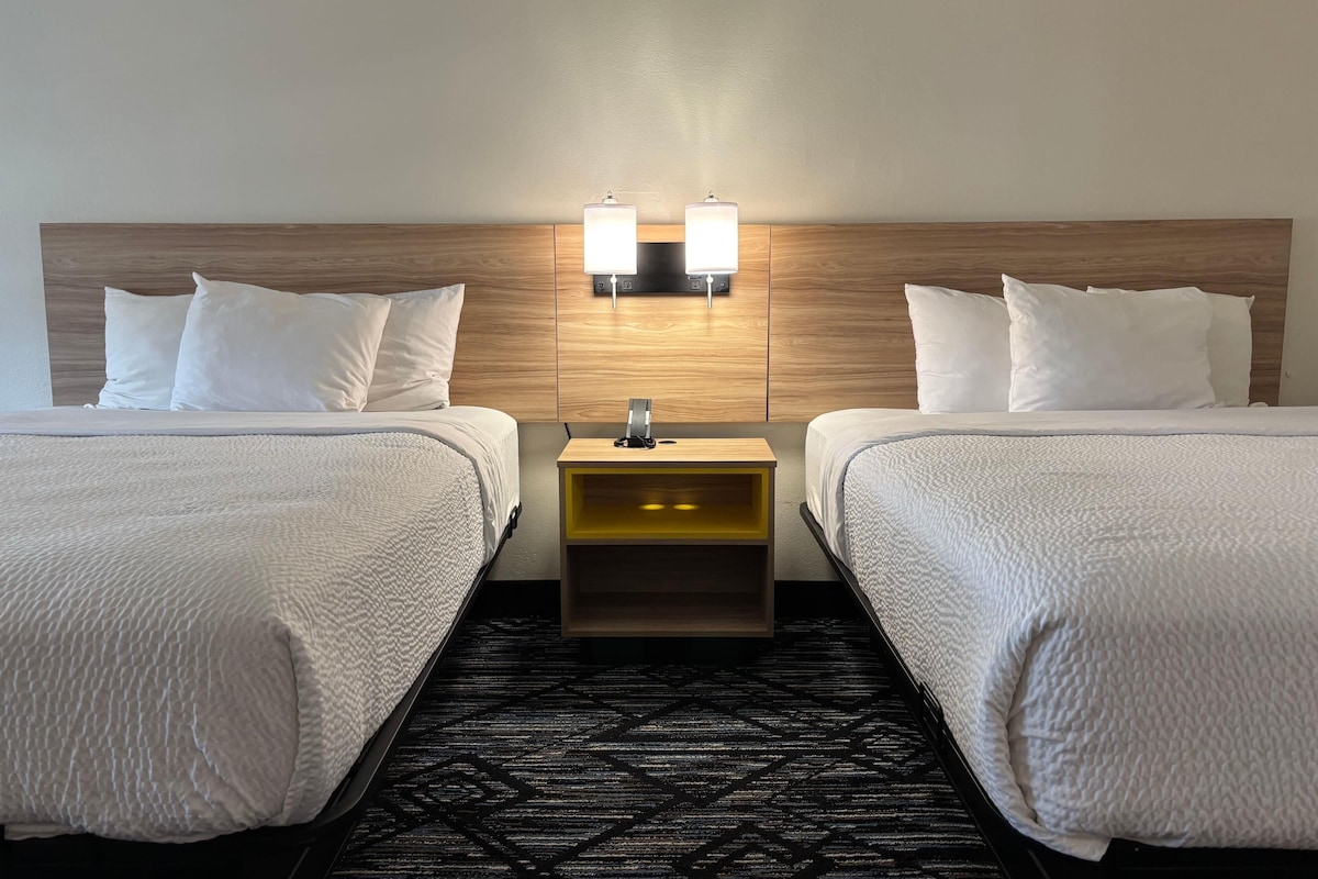 A hotel room with two beds, a nightstand with a lamp, and a patterned carpet.