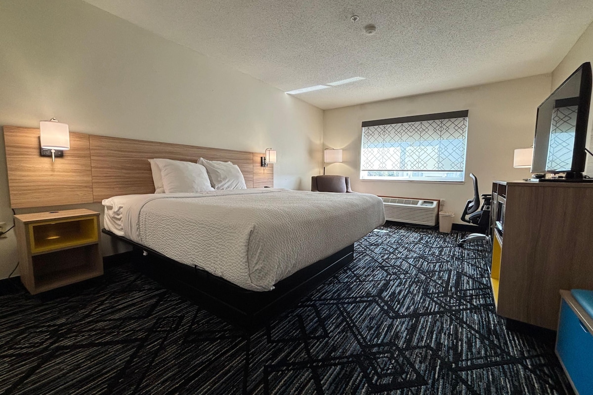 A hotel room with a bed, bedside tables, a desk, a TV, and a window with a view.