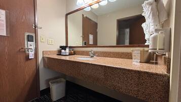 A hotel bathroom with a granite countertop, a sink, a mirror, a towel rack, and a trash bin.