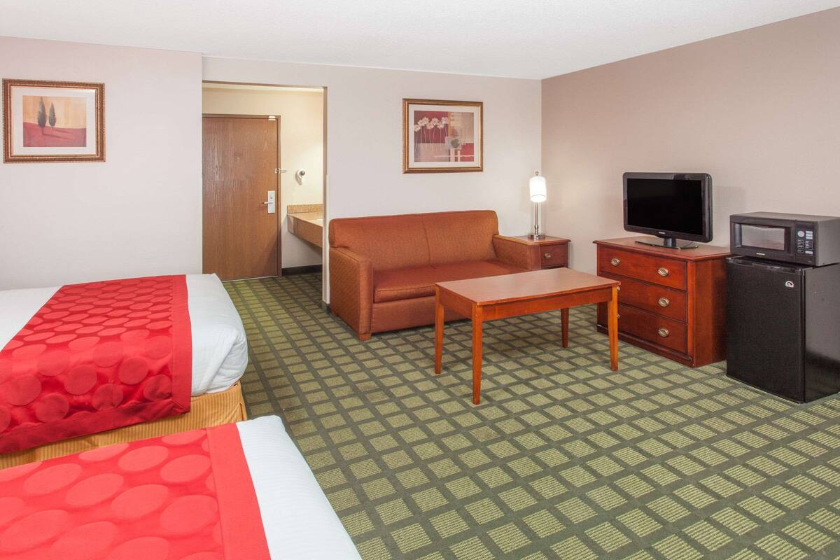 A hotel room with a bed, a sofa, a small table, a TV, a microwave, and a refrigerator.