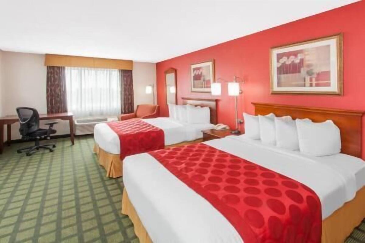 A hotel room with two beds, a desk, a chair, and a window with curtains.