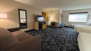 Une chambre d’hôtel avec un canapé, une télévision, un bureau avec une lampe, une fenêtre et un tapis à motifs.