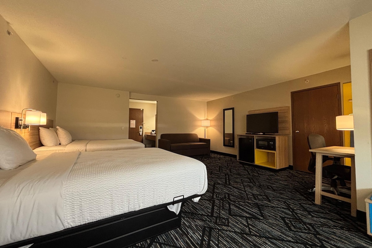 A hotel room with two beds, a desk, a TV, and a door.