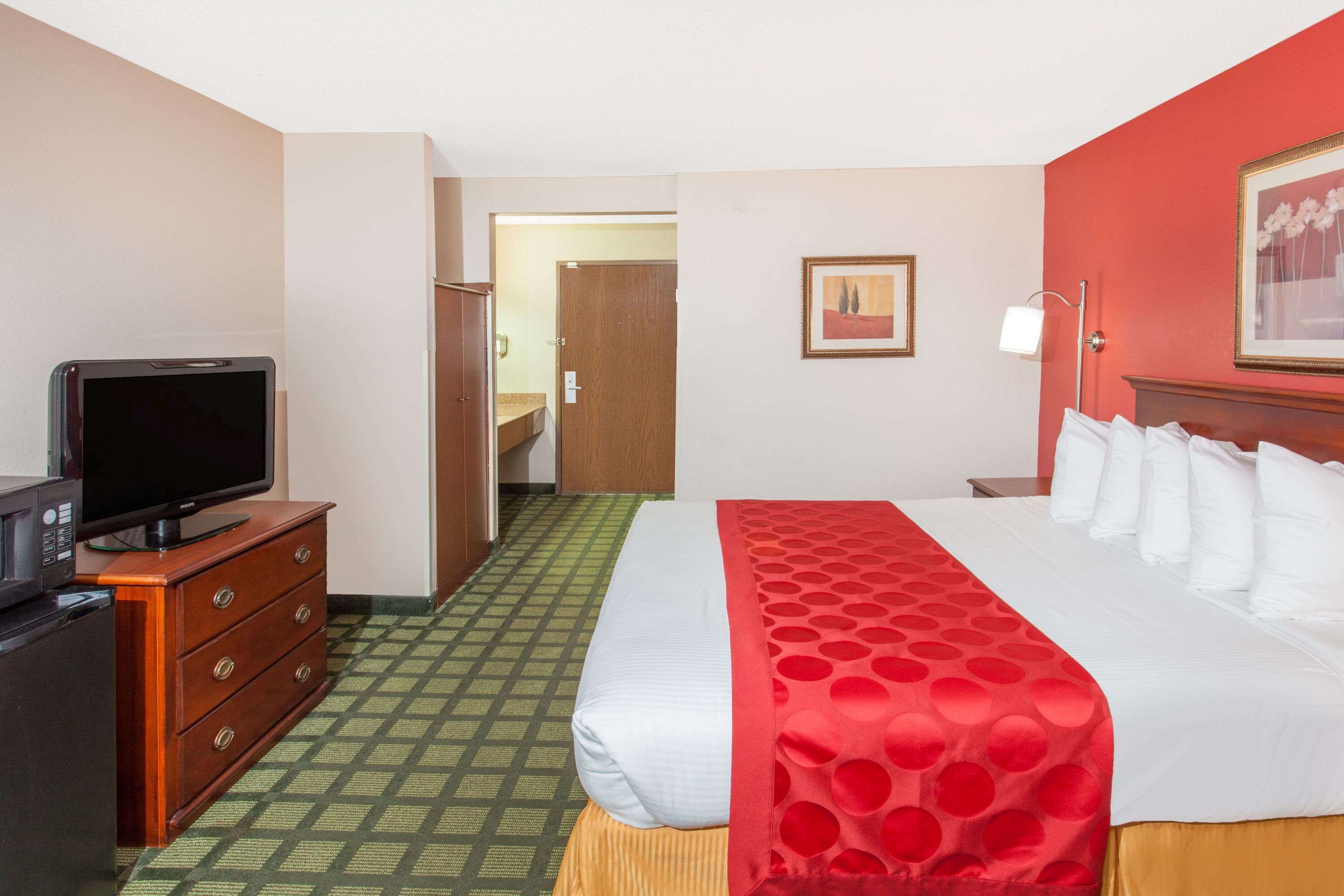 Une chambre d’hôtel avec un lit, un téléviseur posé sur une commode, une porte donnant sur une autre pièce et un tableau encadré accroché au mur.