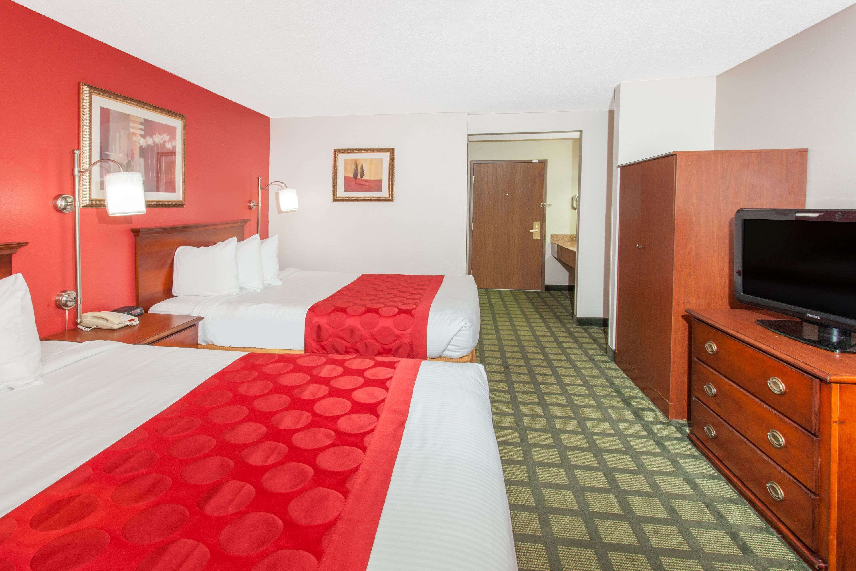 Quarto de hotel com duas camas, uma televisão sobre um criado-mudo e uma porta que dá para outro espaço.