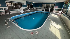 Une piscine intérieure avec un sol carrelé, des chaises longues et un panneau indiquant qu’il est interdit de plonger.