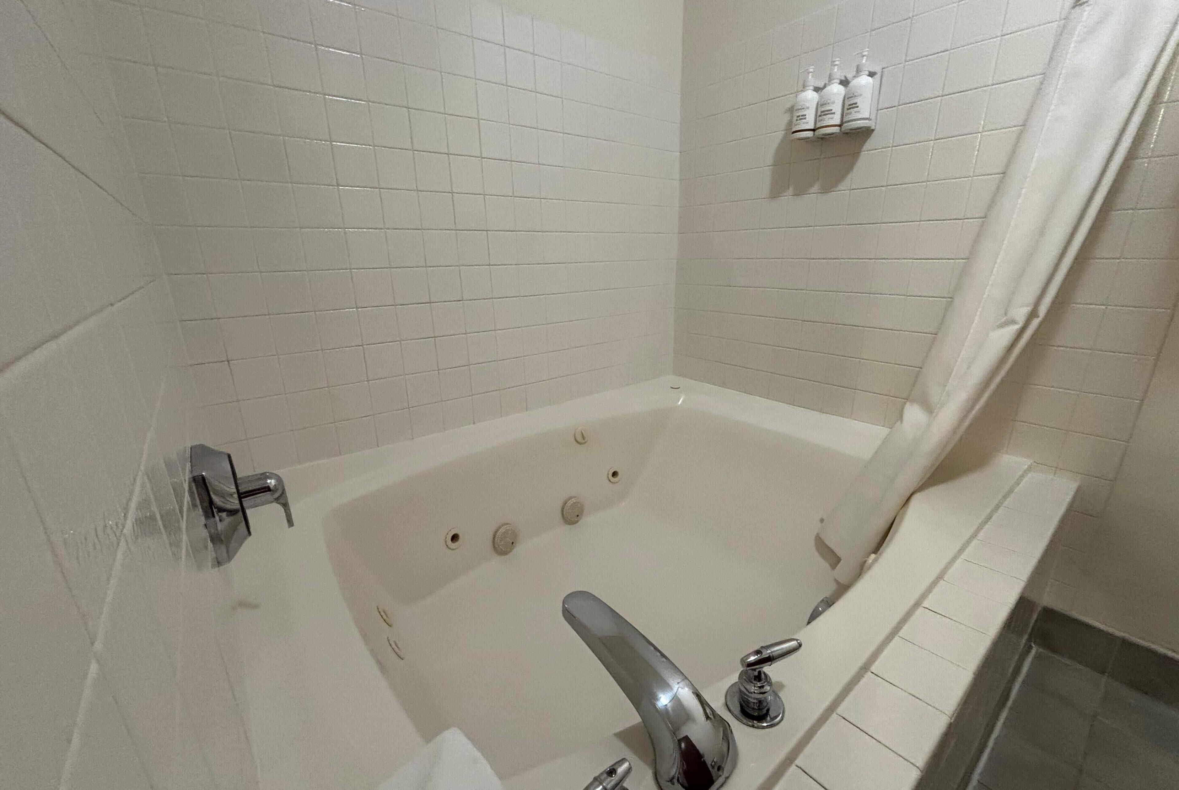 A bathroom with a bathtub, a shower curtain, and a shelf with toiletries.