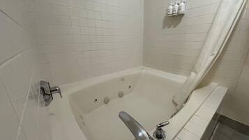 A bathroom with a bathtub, a shower curtain, and a shelf with toiletries.