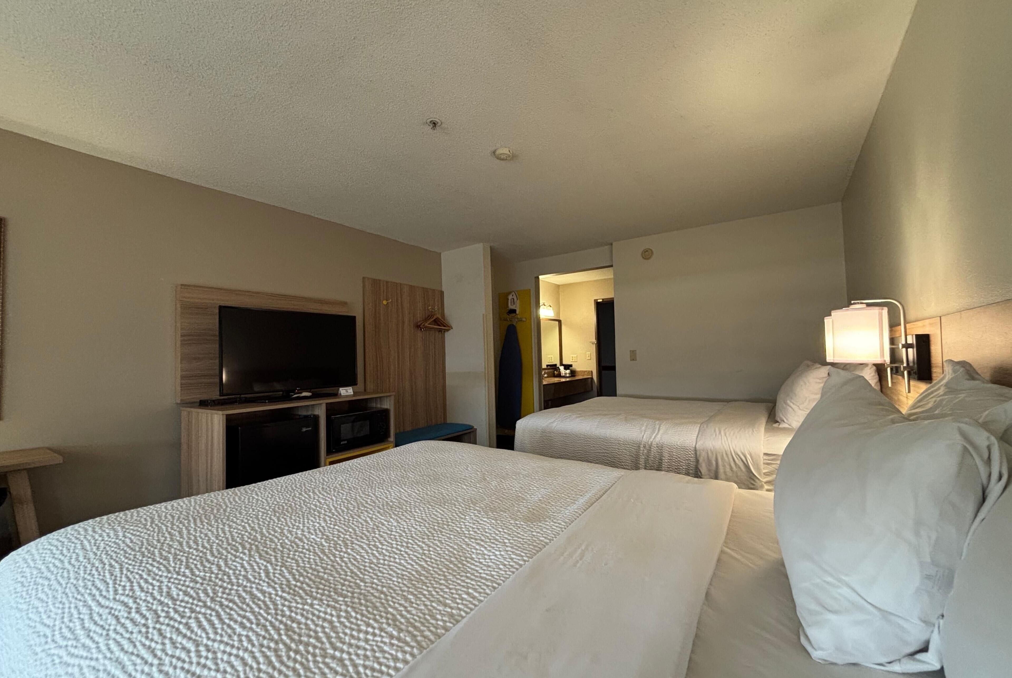 A hotel room with two beds, a television, a desk, and a mirror.