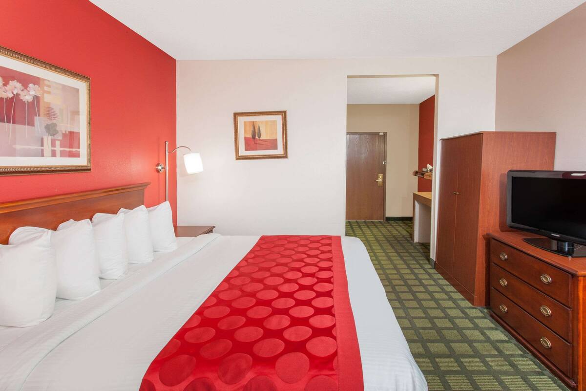 A hotel room with a bed, a television on a wooden dresser, and a door leading to a bathroom.