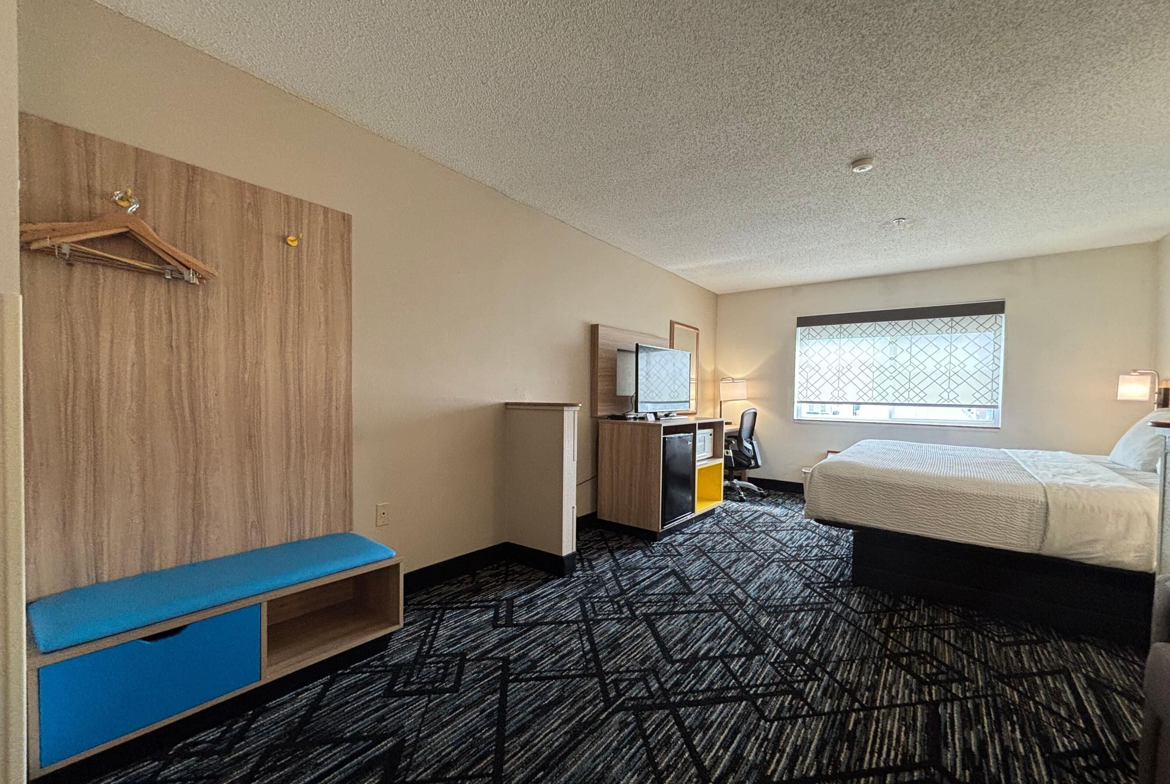 Een hotelkamer met een bed, een bureau met computer, een televisie, een kledingkast en een raam met uitzicht.
