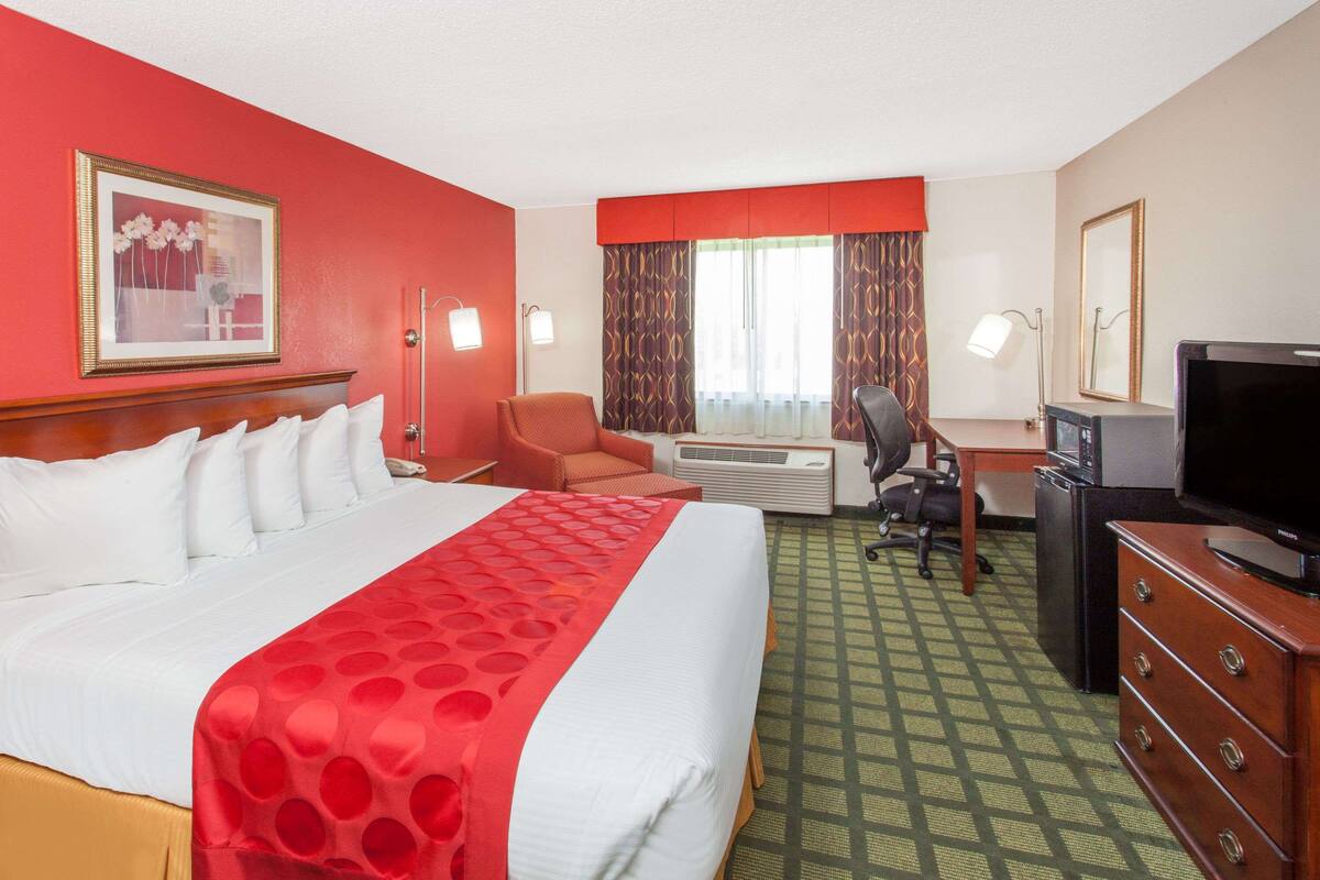 A hotel room with a large bed, a desk with a computer, a television, and a window with curtains.