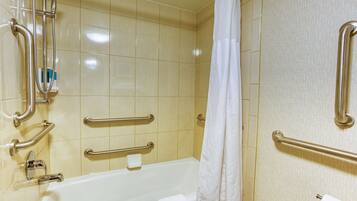 A bathroom with a bathtub, grab bars, a showerhead, and a toilet paper holder.
