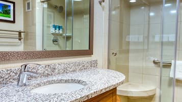 Une salle de bain moderne avec un lavabo sur un plan de travail en granit, un miroir et une douche à parois de verre.