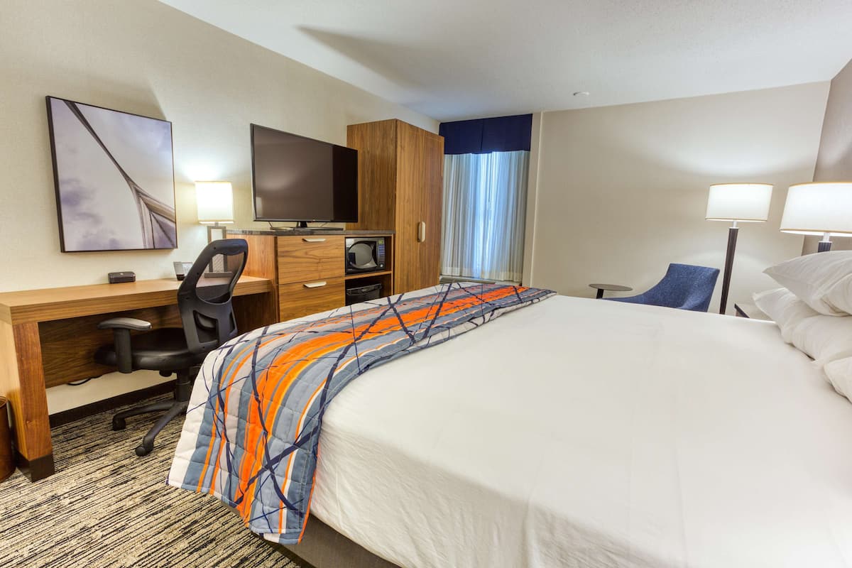 A hotel room with a bed, desk, chair, TV, and lamps.