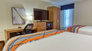 A hotel room with two beds, a desk with a computer, a television, and a window with curtains.