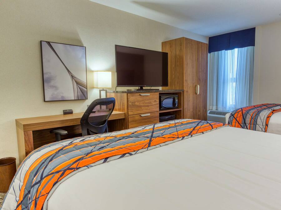 A hotel room with two beds, a desk with a computer, a television, and a window with curtains.