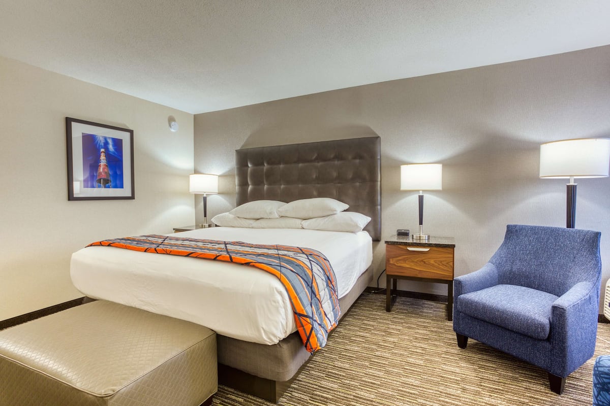 A hotel room with a bed, a chair, a nightstand, and a picture on the wall.