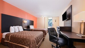 A hotel room with two beds, a desk, a chair, a television, and a window with curtains.