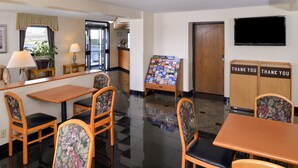 A hotel lobby with wooden furniture, a reception desk, a display board, and a television on the wall.