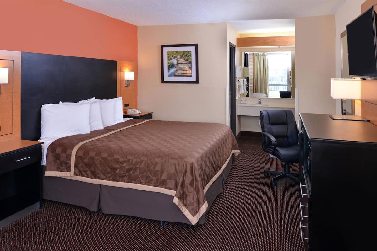 Habitación de hotel con una cama grande, un escritorio con silla, televisión y baño visible a través de una puerta abierta.