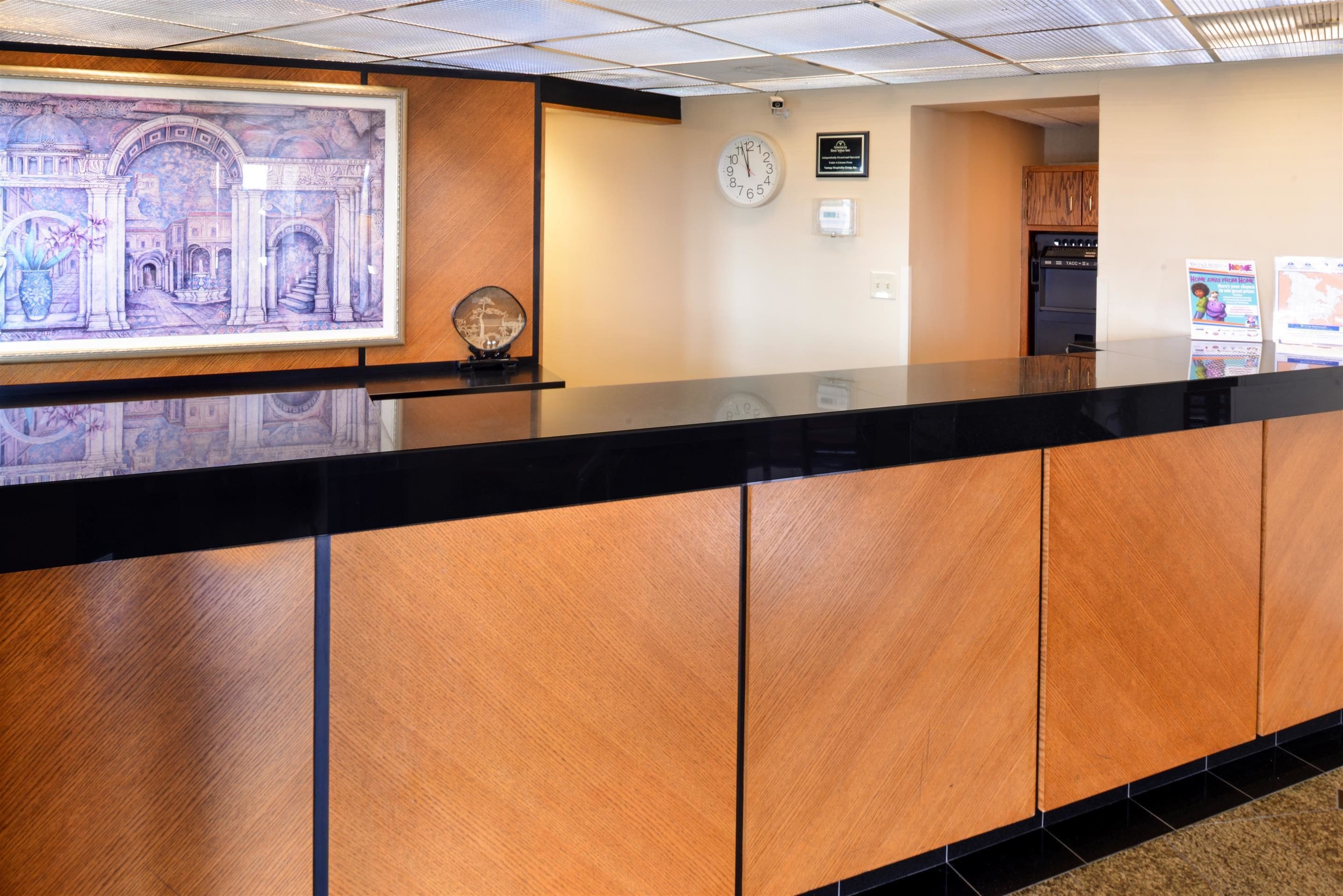 A reception area with a wooden counter, a clock, and a framed mural on the wall.
