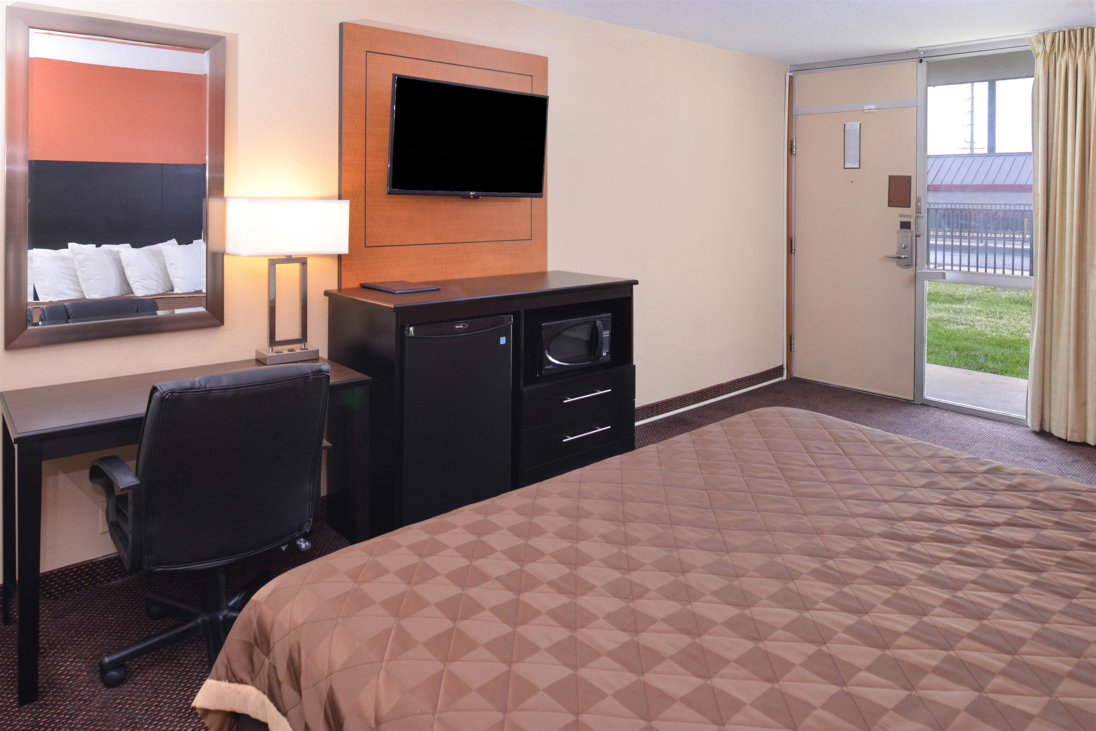 A hotel room with a bed, desk, chair, TV, and a sliding door to the outside.