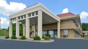 A hotel with a covered entrance, a red roof, and a parking lot.