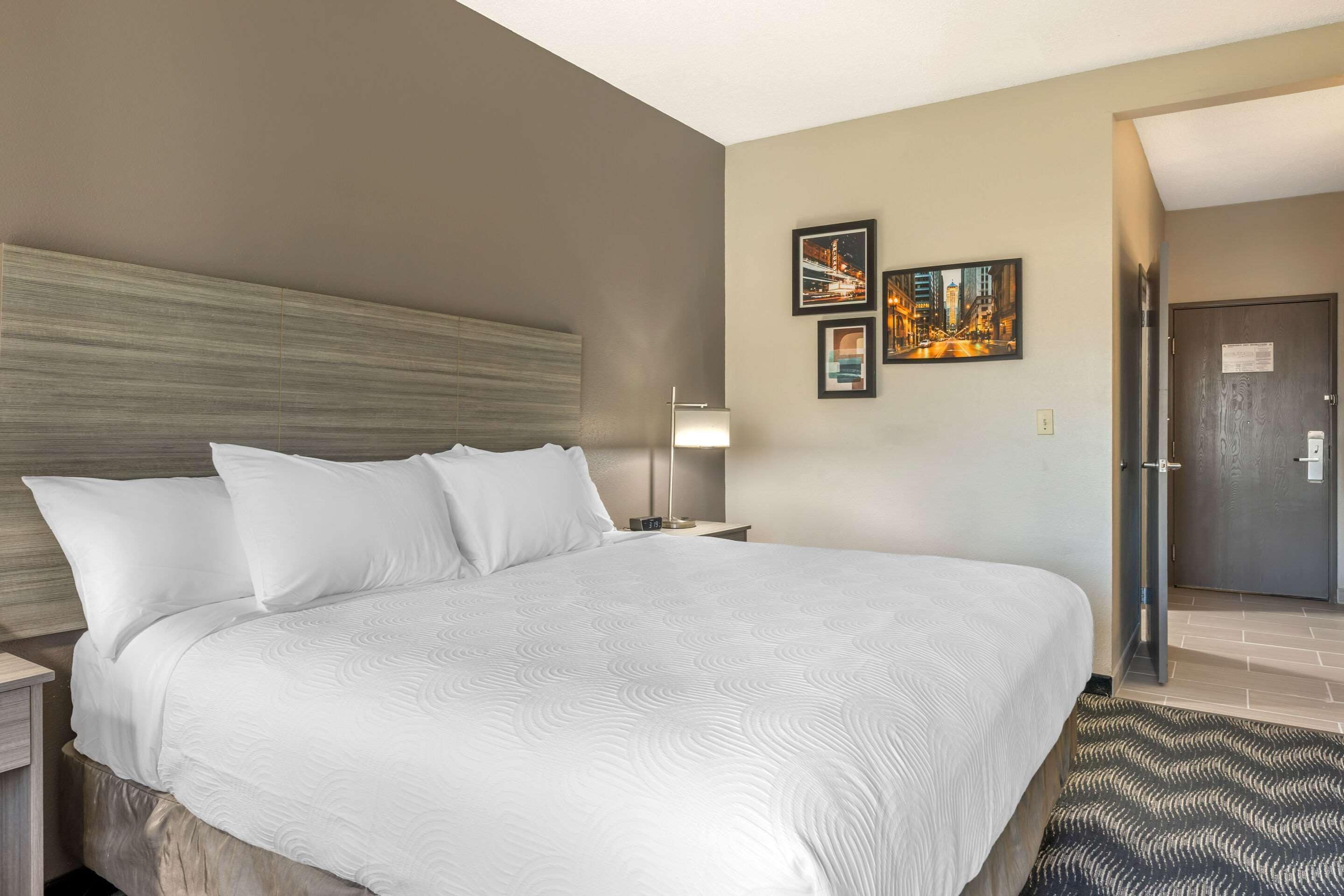 Una habitación de hotel con una cama grande, una mesita de noche, una lámpara y una puerta.