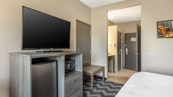 A hotel room with a flat-screen TV, a mini-fridge, a microwave, a bed, a desk, and a chair.