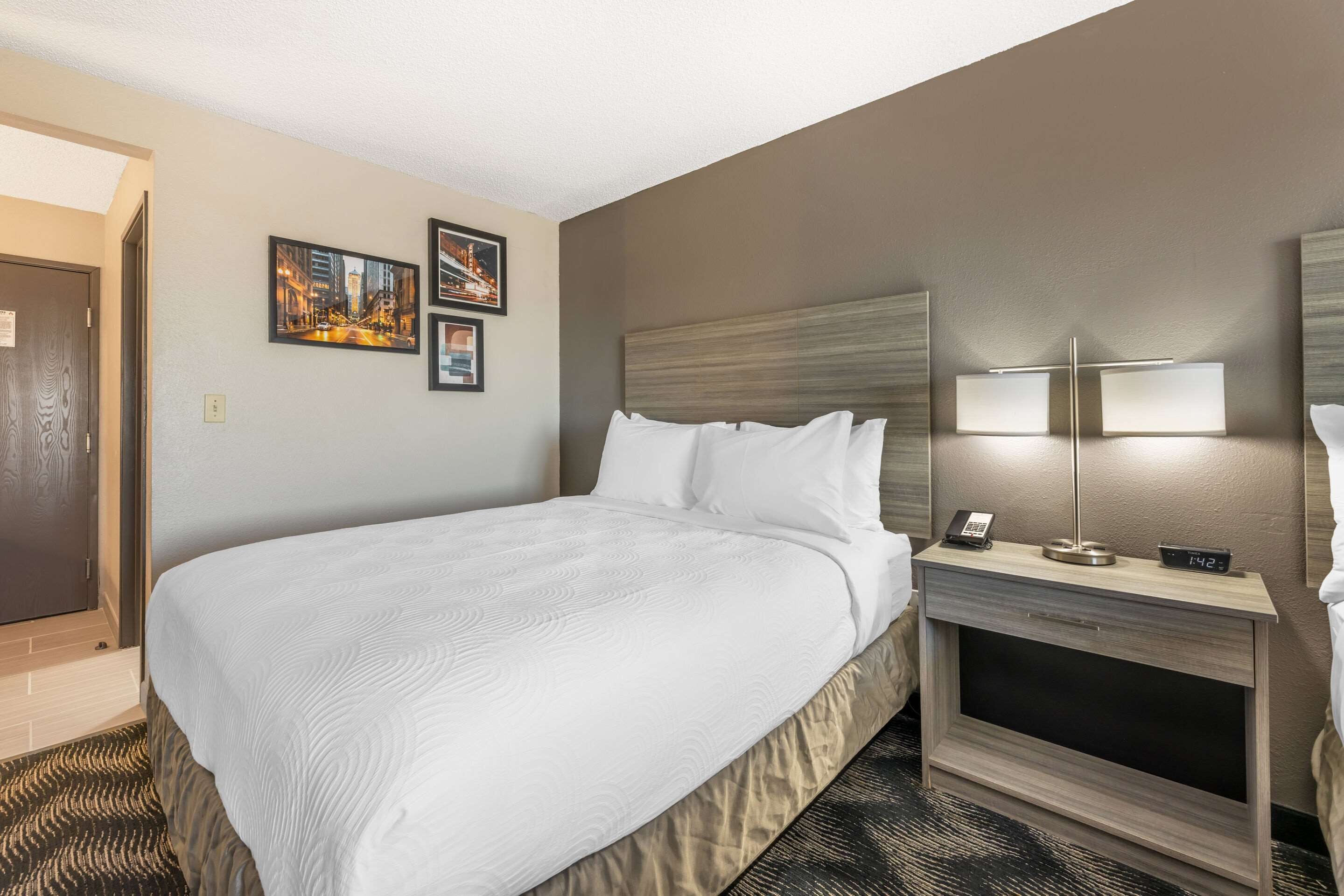 A hotel room with a large bed, a bedside table with a lamp, and two framed pictures on the wall.