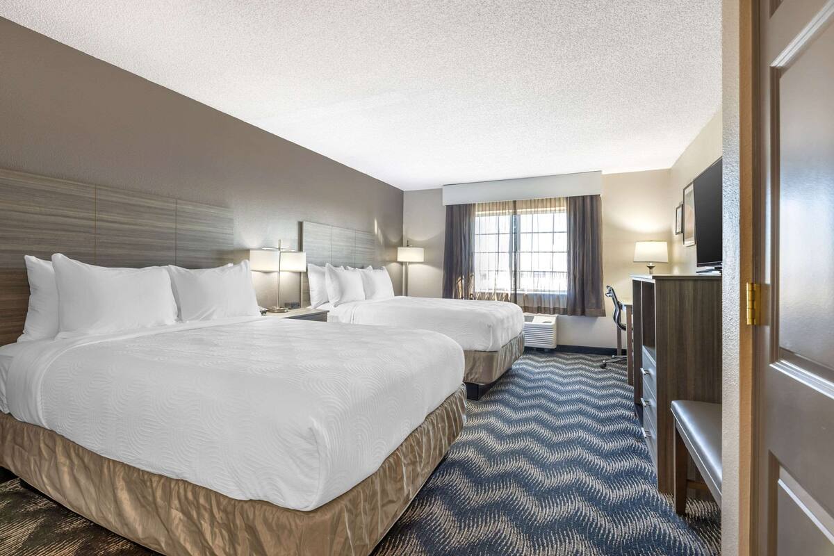 A hotel room with two beds, a desk, a TV, and a window with curtains.