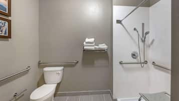 Un baño con inodoro, ducha con barras de apoyo y toallero.