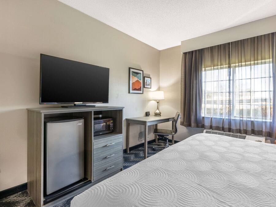 A hotel room with a bed, a desk, a television, a refrigerator, and a window with curtains.