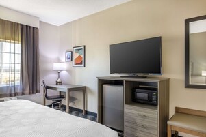 Habitación de hotel con cama, escritorio con silla, televisor, microondas y refrigerador.