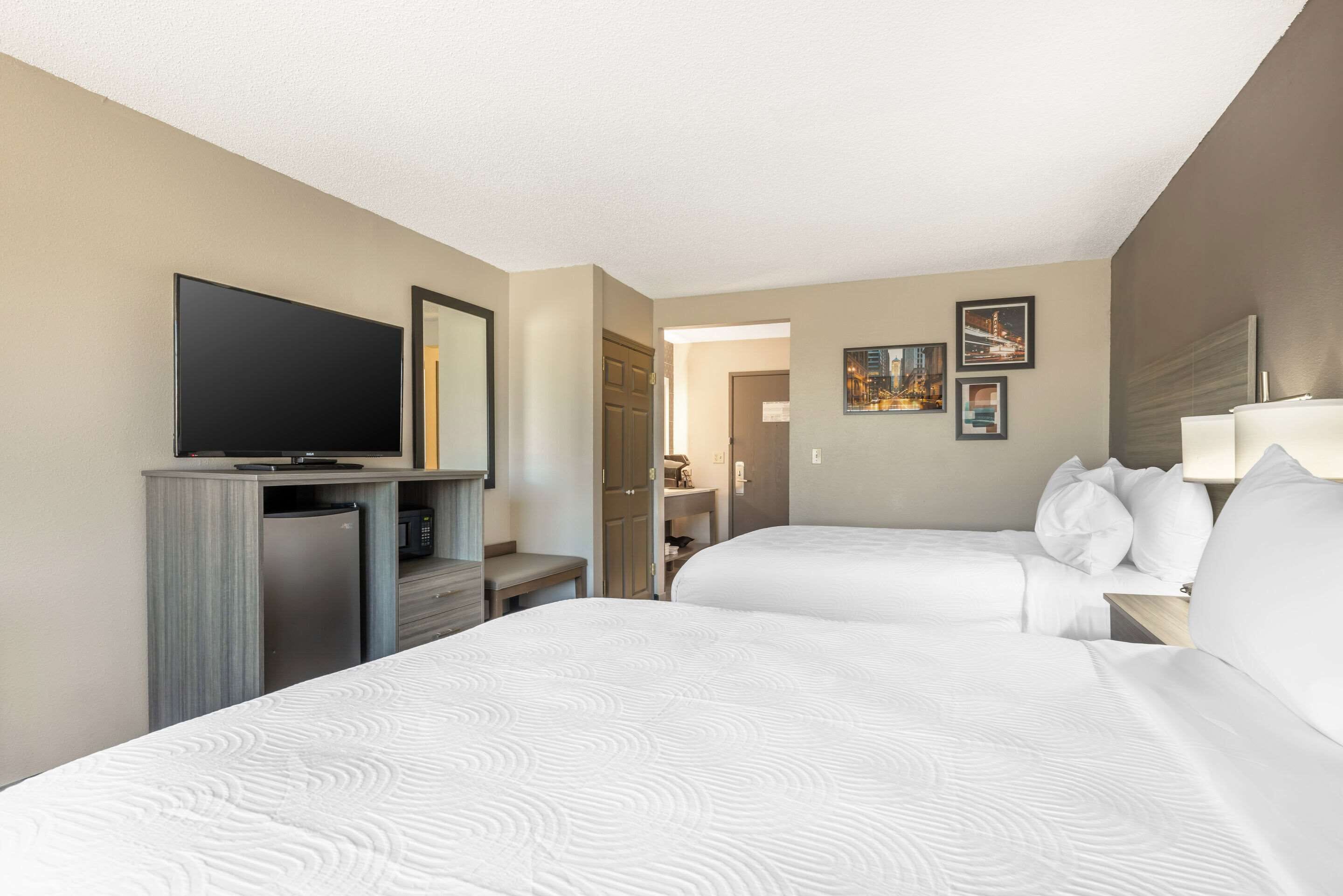 Ein Hotelzimmer mit zwei Betten, einem Fernseher, einer Minibar und einem durch eine geöffnete Tür einsehbarer Badezimmer.