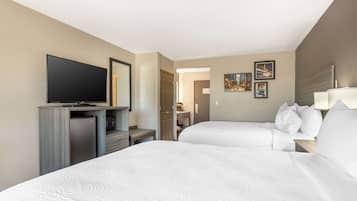 Ein Hotelzimmer mit zwei Betten, einem Fernseher, einer Minibar und einem durch eine geöffnete Tür einsehbarer Badezimmer.