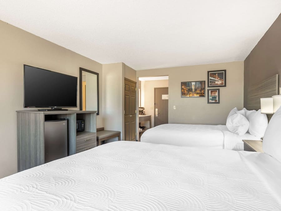 Ein Hotelzimmer mit zwei Betten, einem Fernseher, einer Minibar und einem durch eine geöffnete Tür einsehbarer Badezimmer.