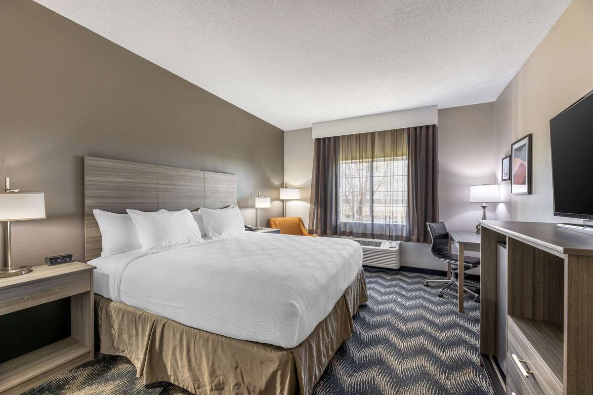 A hotel room with a large bed, a desk with a chair, a television, and a window with curtains.