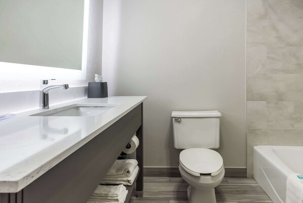 Un baño moderno con un lavamanos, espejo y retrete blancos, además de una bañera.
