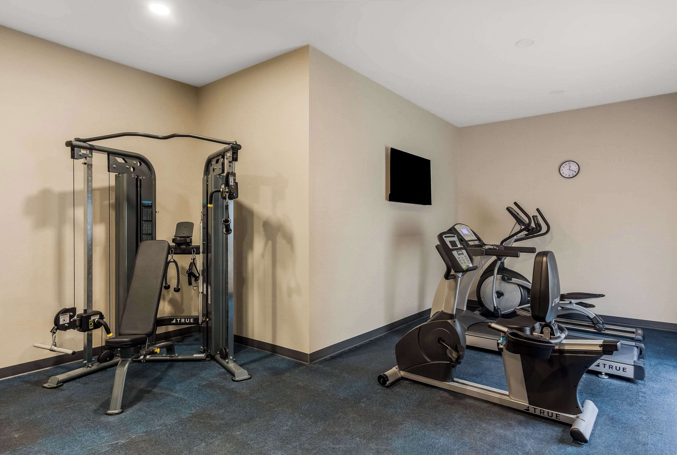 Un gimnasio con una bicicleta estática, una máquina de pesas y un televisor montado en la pared.