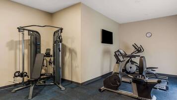 Un gimnasio con una bicicleta estática, una máquina de pesas y un televisor montado en la pared.