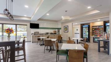 A modern dining area with multiple tables and chairs, a kitchen in the background, and a beverage station.